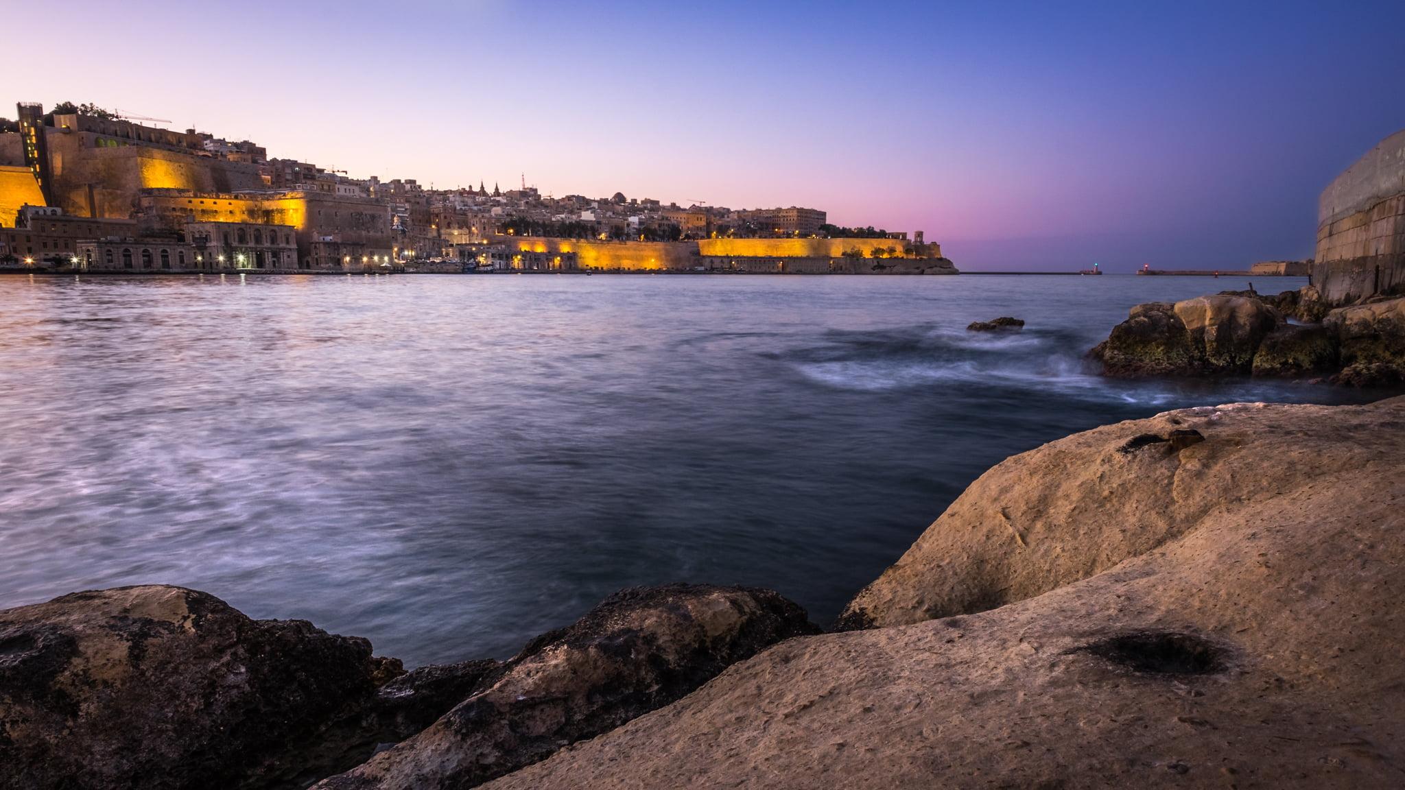 Architectural photo of concrete houses near body of water, valletta