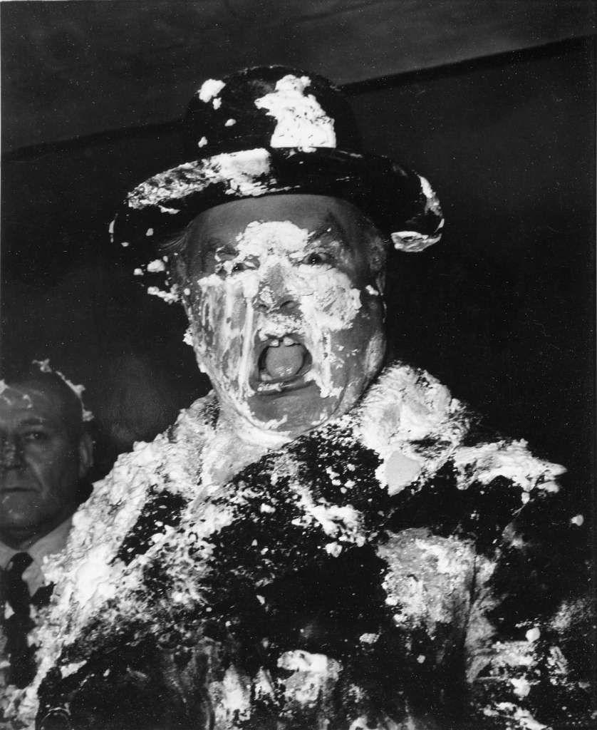 A man’s face is covered in cream as a result of a pie fight in the